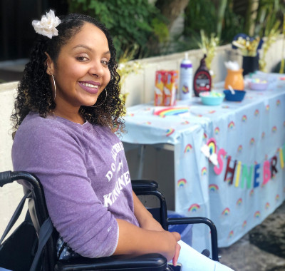 Portrait of a student with a purple shirt and flower in her hair sitting in a wheelchair