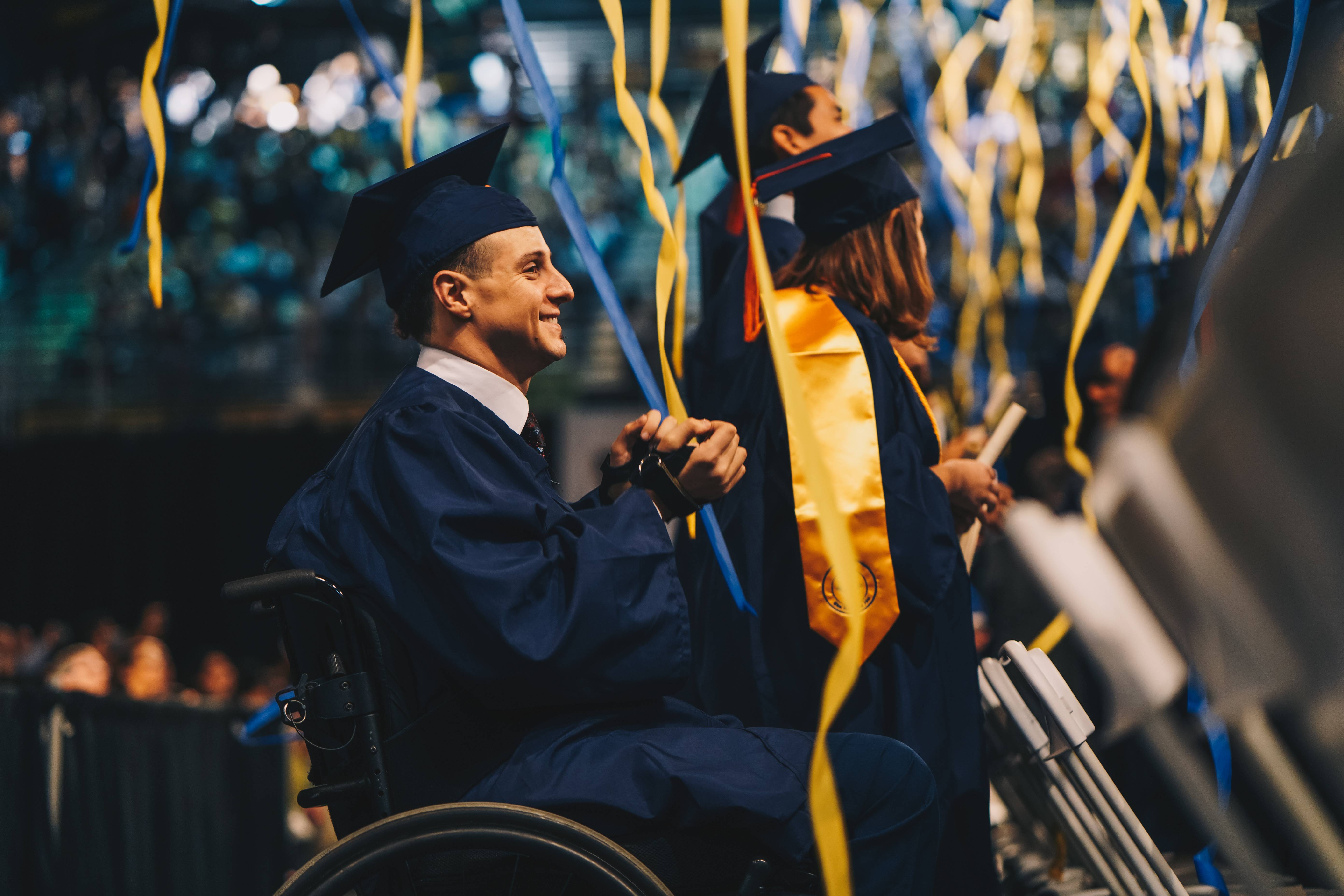 Male graduate in a wheelchair clapping during graduation